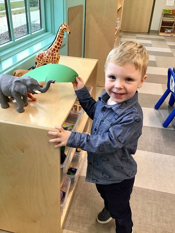 Child playing with toy elephant and green paper in a classroom