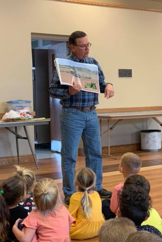 Person holding a large book with images, speaking to a group of children