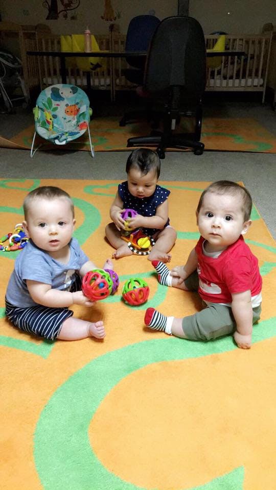 Three babies sitting on a rug with toys