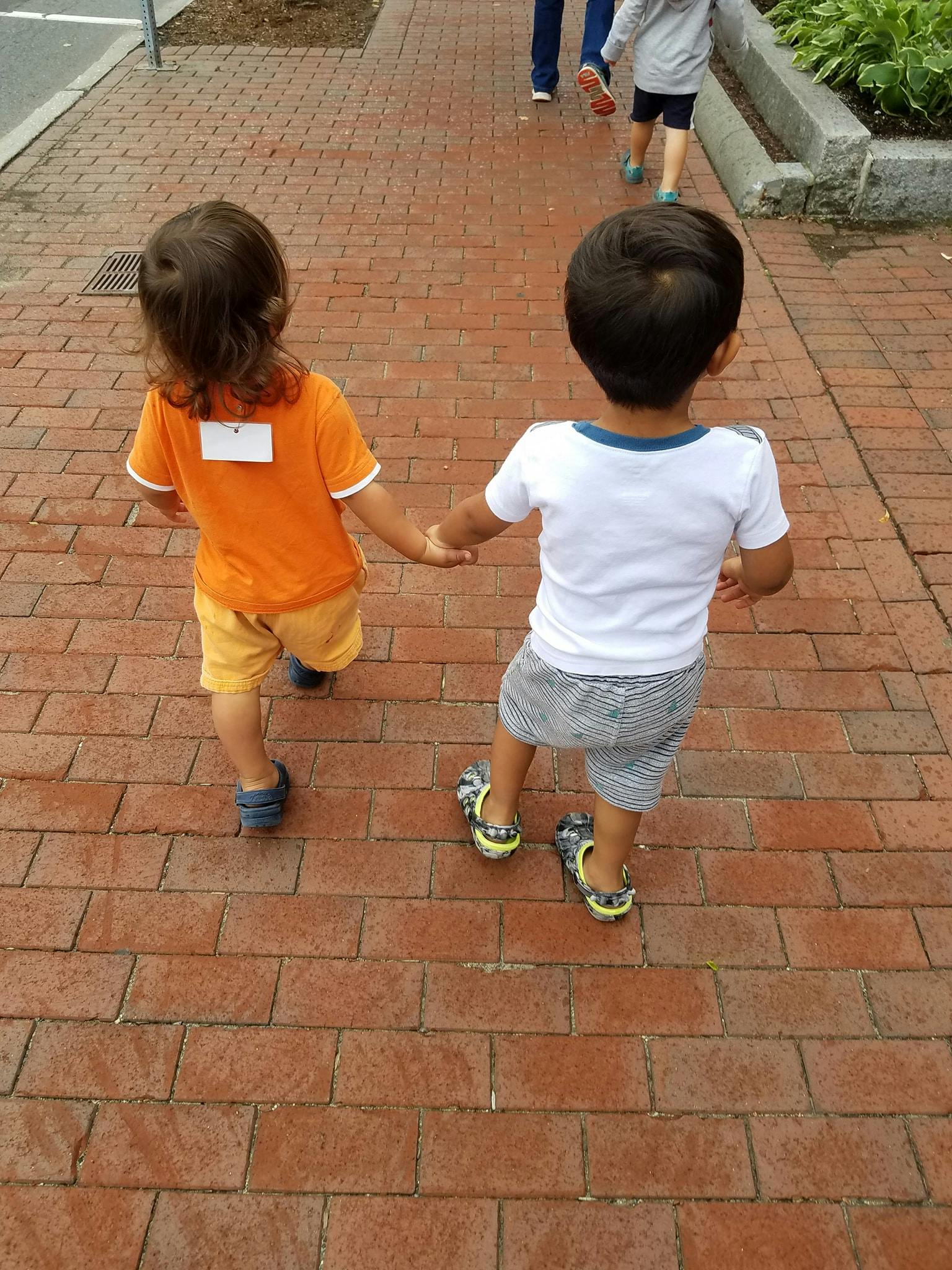 Two children holding hands and walking on a brick path