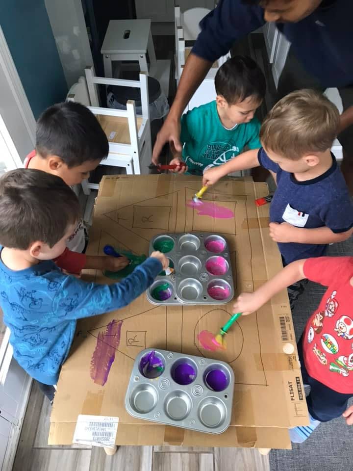 Adult and children painting on cardboard with muffin tins of paint