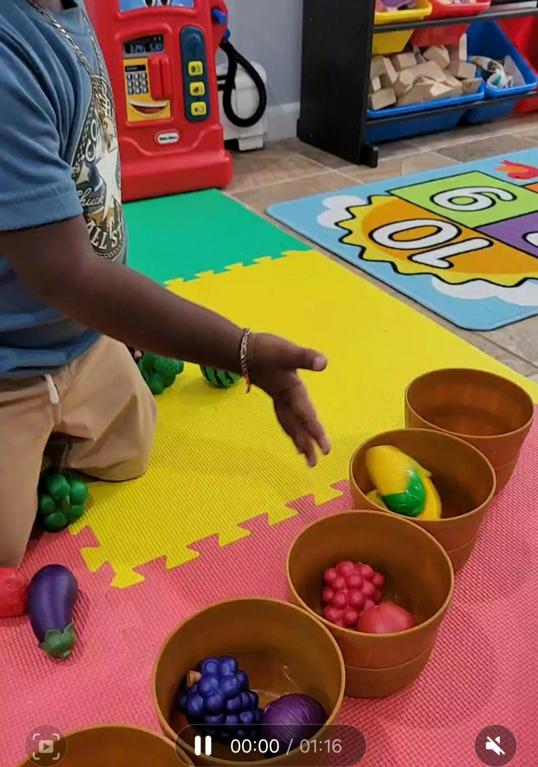 Child on floor reaching for toy fruit in cups