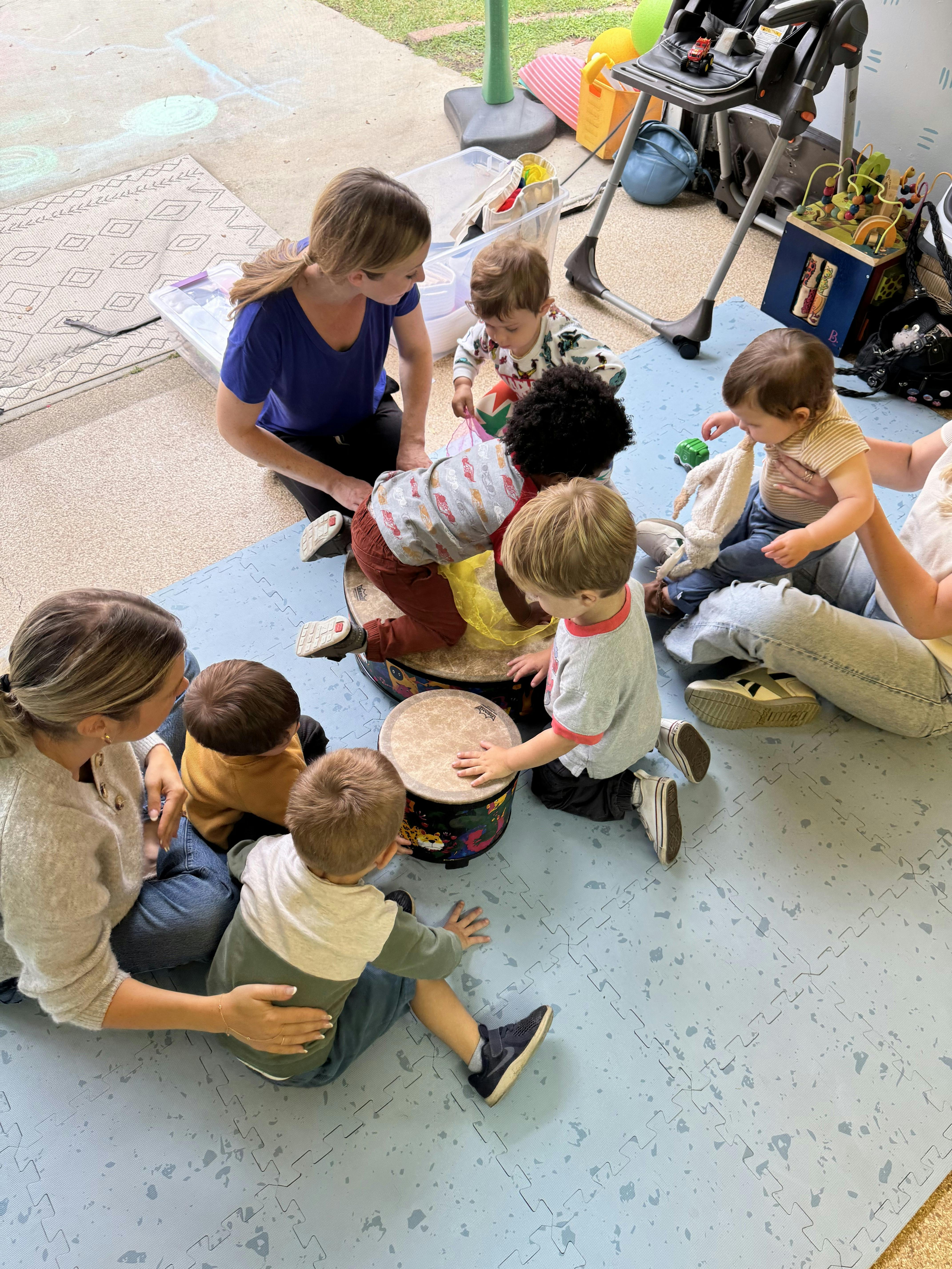 People sitting on floor mats playing drums in a classroom setting