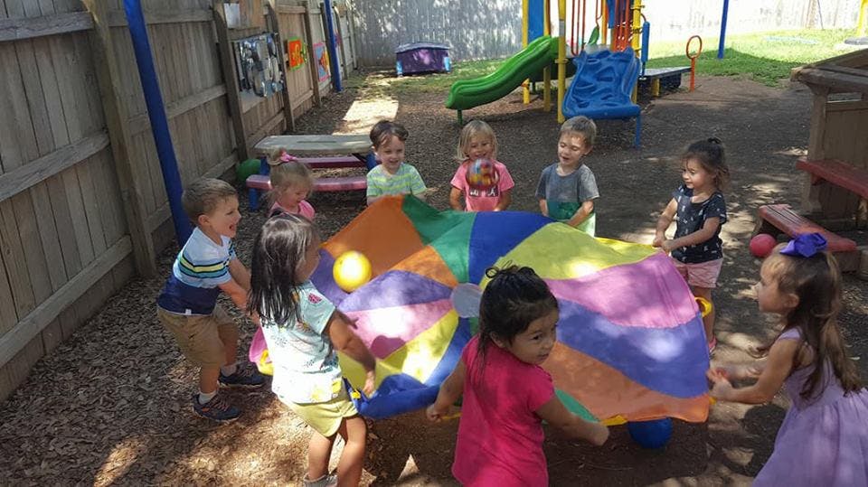 Children playing with a colorful parachute and ball outdoors