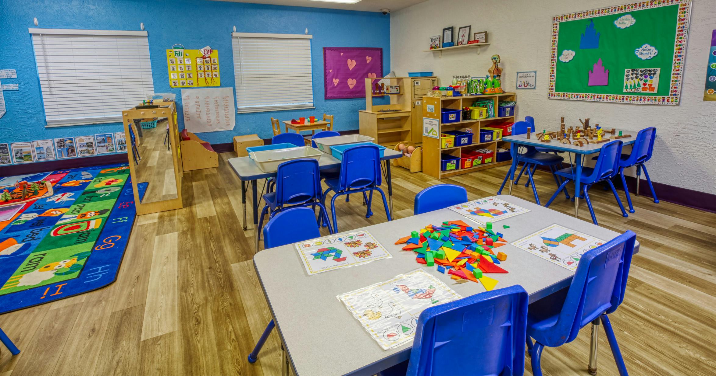 Classroom with tables, blue chairs, learning rug, and educational displays