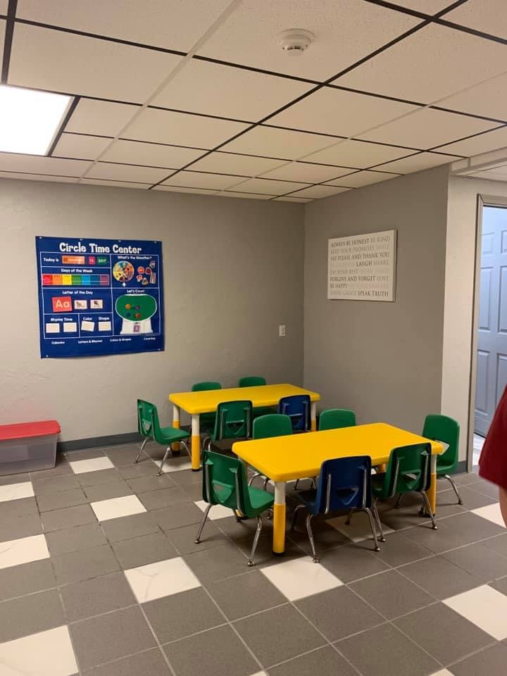 Classroom with yellow tables and green chairs, "Circle Time Center" poster on wall