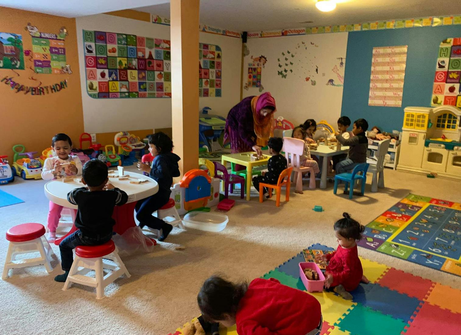 Children and adults in a classroom with tables and play mats