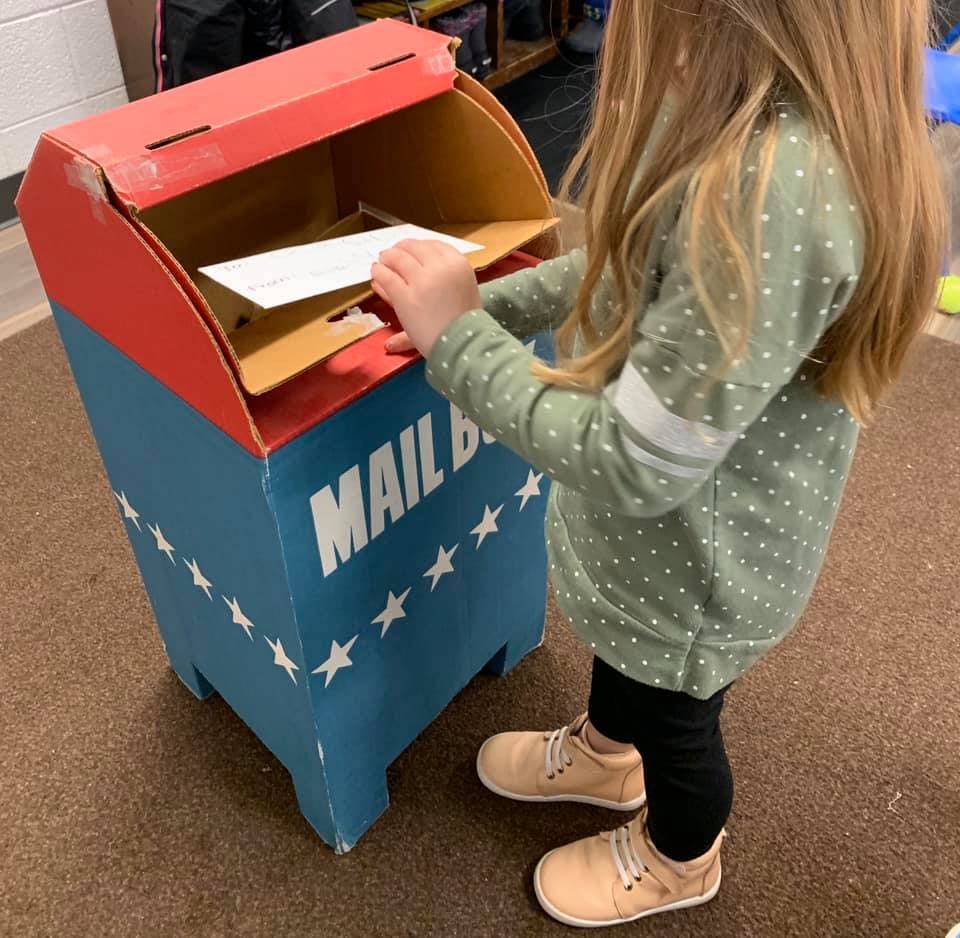 Child putting a letter into a toy mailbox