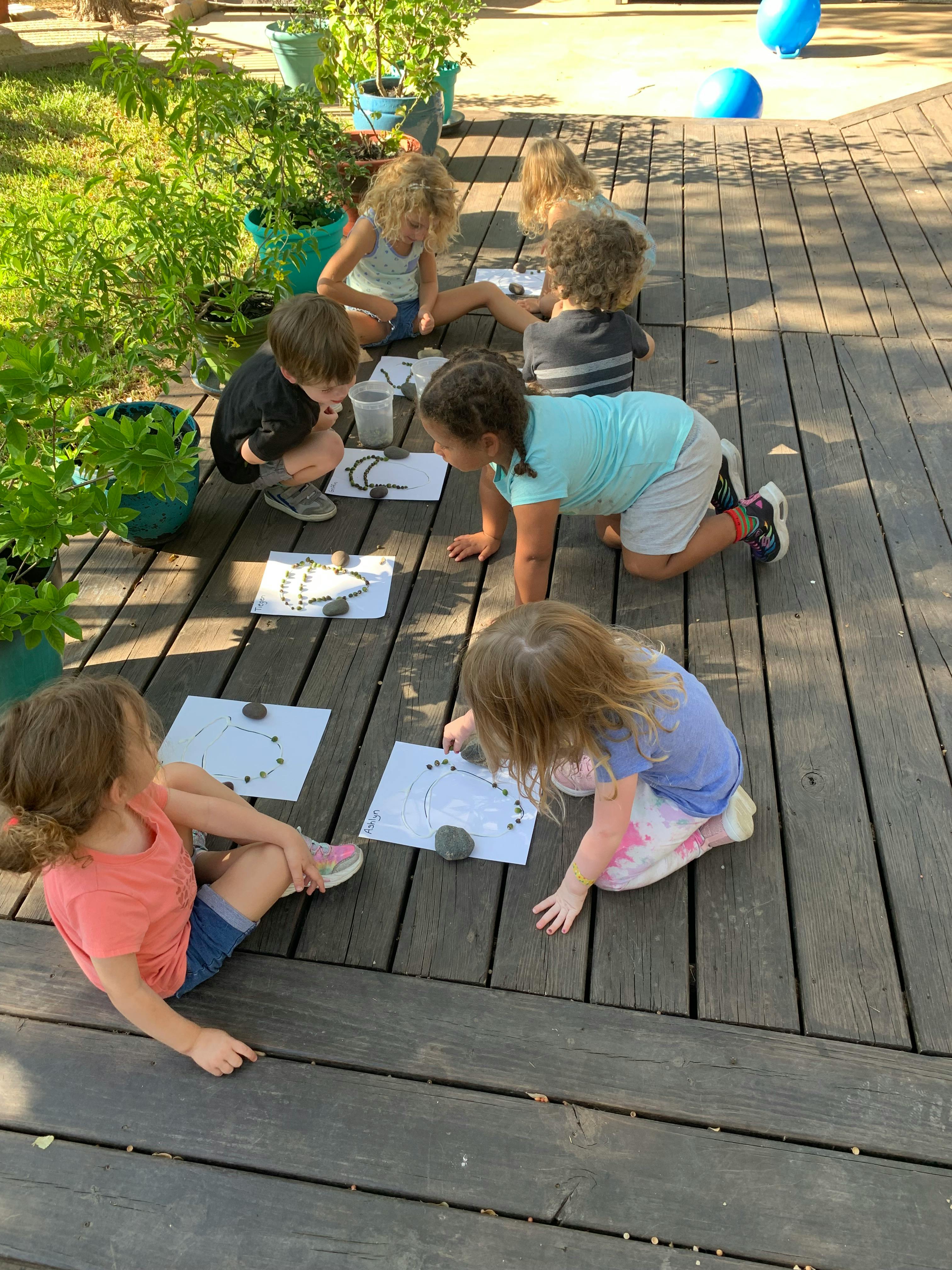 Children on a wooden deck arranging small objects on paper