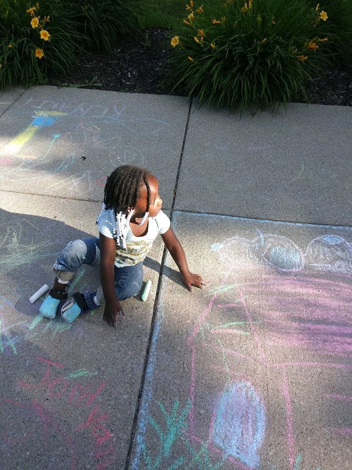 Child kneeling on a sidewalk drawing with chalk