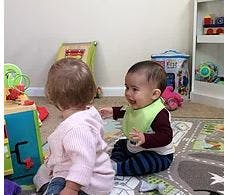 Two babies playing on a rug