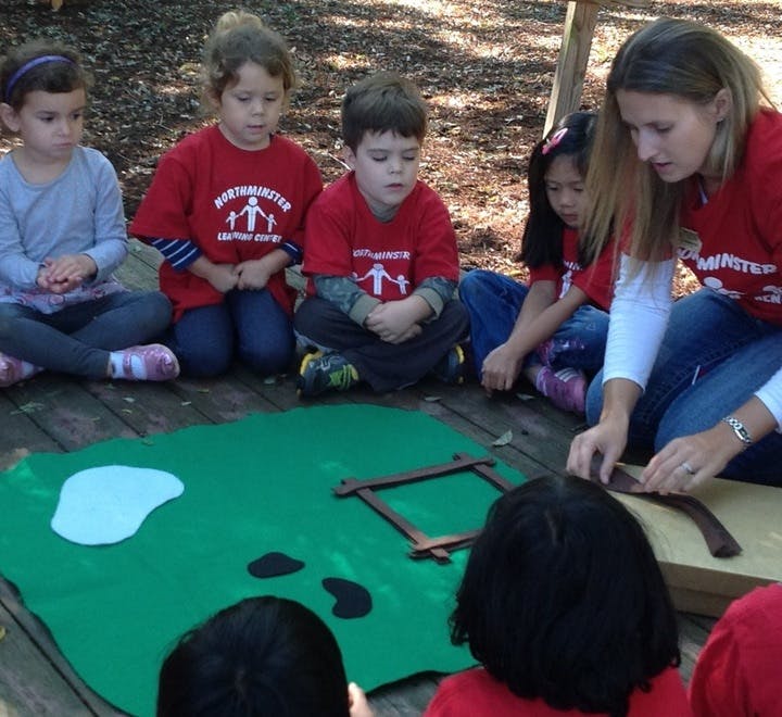 Adult and children sitting on a wooden deck, looking at items on a green mat