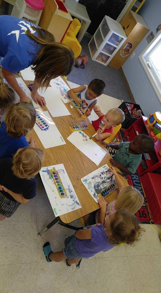 Adult and children painting at a table in a classroom
