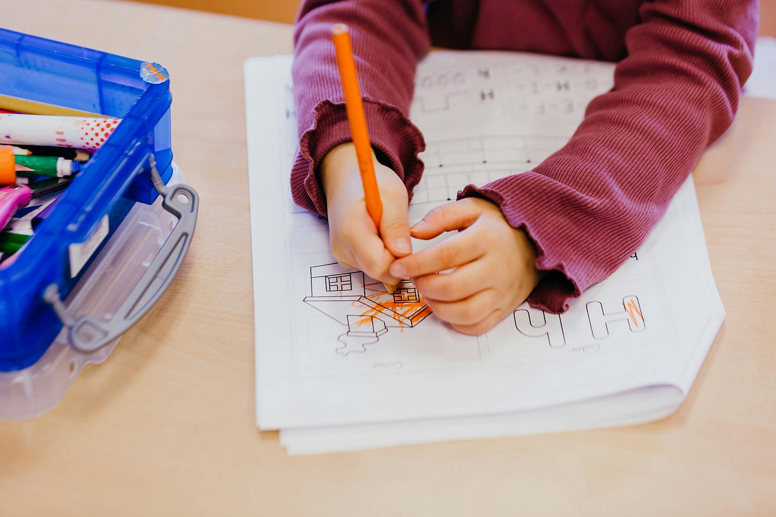 Child's hands coloring a drawing with an orange pencil