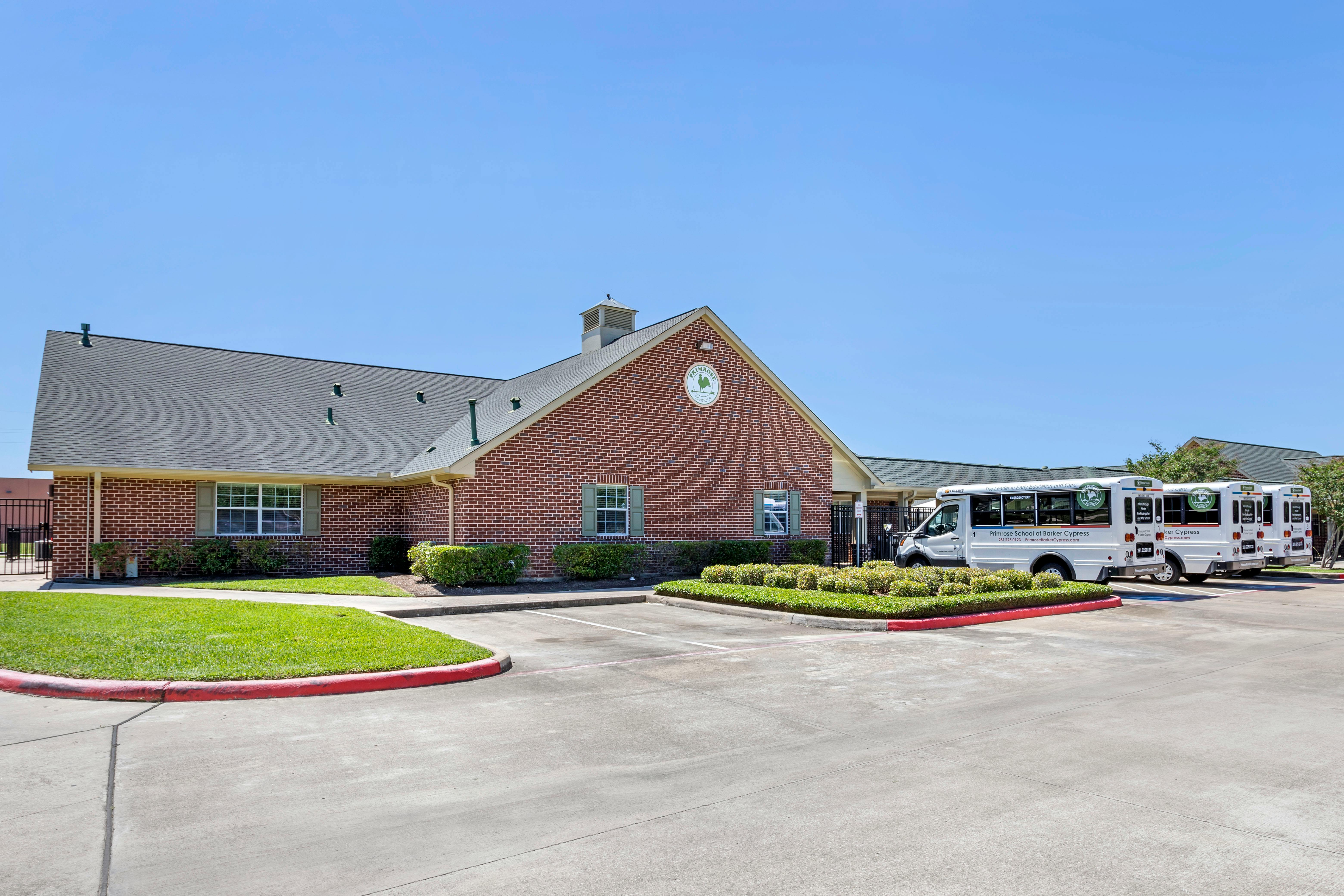 Primrose School building with a "Primrose Schools" logo on the facade and three white buses