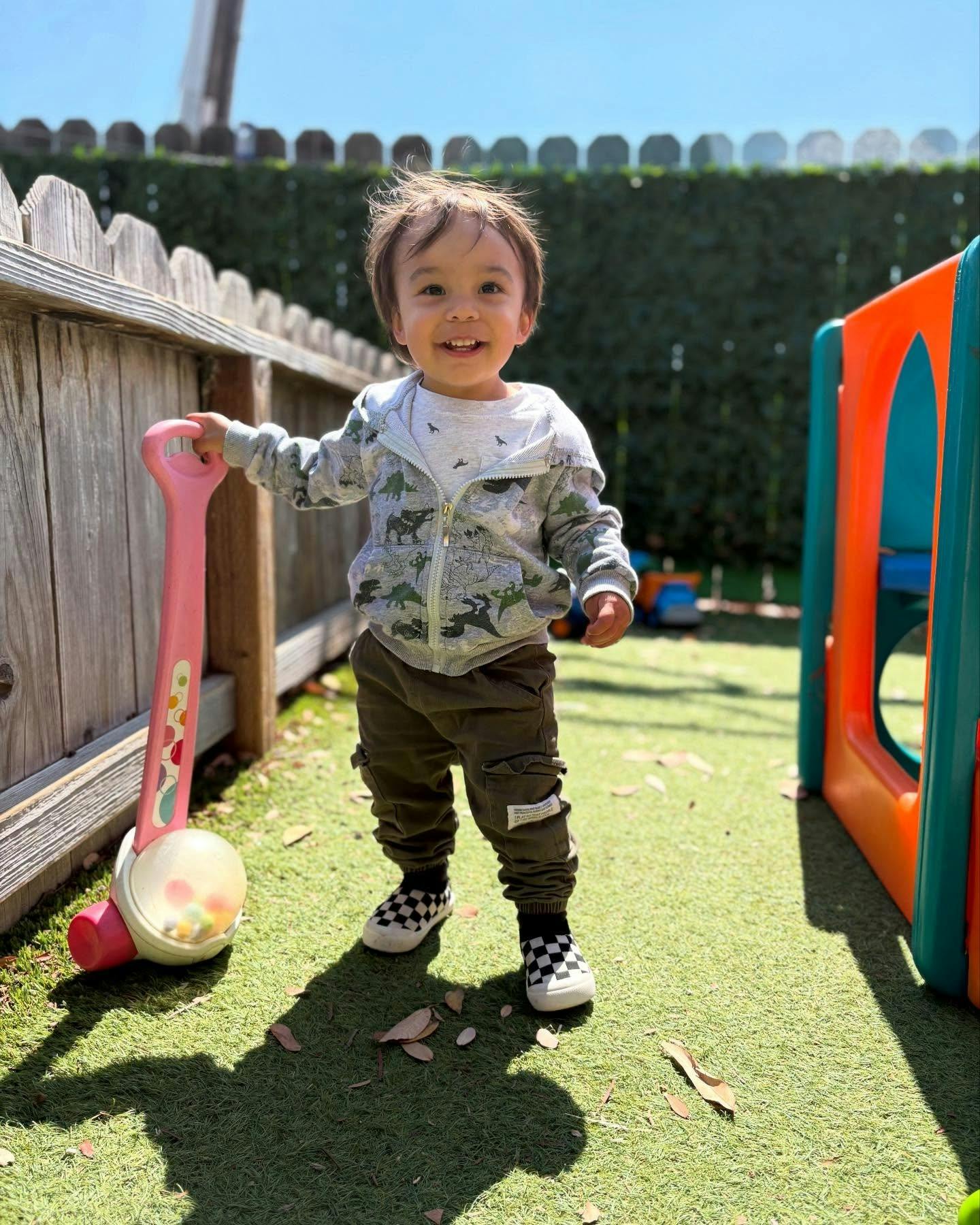 A child standing in a yard holding a push toy
