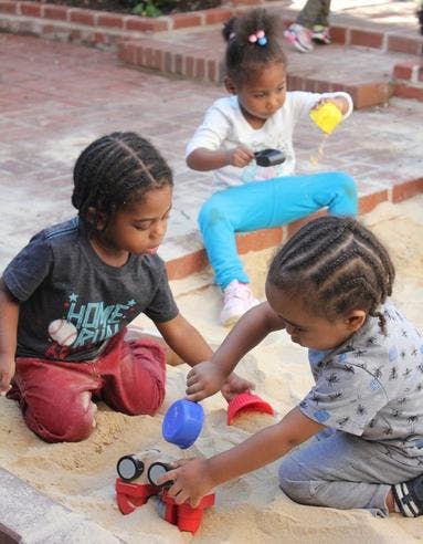 Three children playing in a sandbox with toys