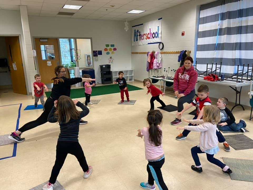 Adults and children exercising in a room with "Afterschool" on the wall