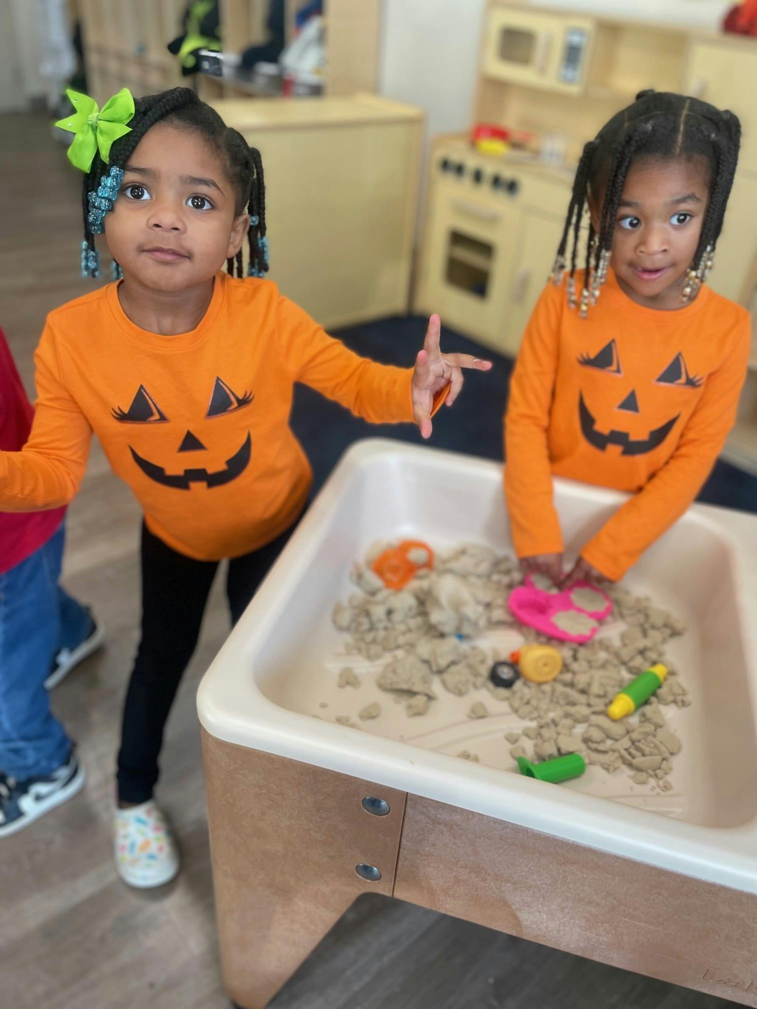 Two children in pumpkin shirts playing with sand and toys in a sensory bin