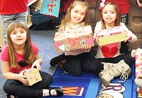 Three children sitting on the floor holding decorated boxes