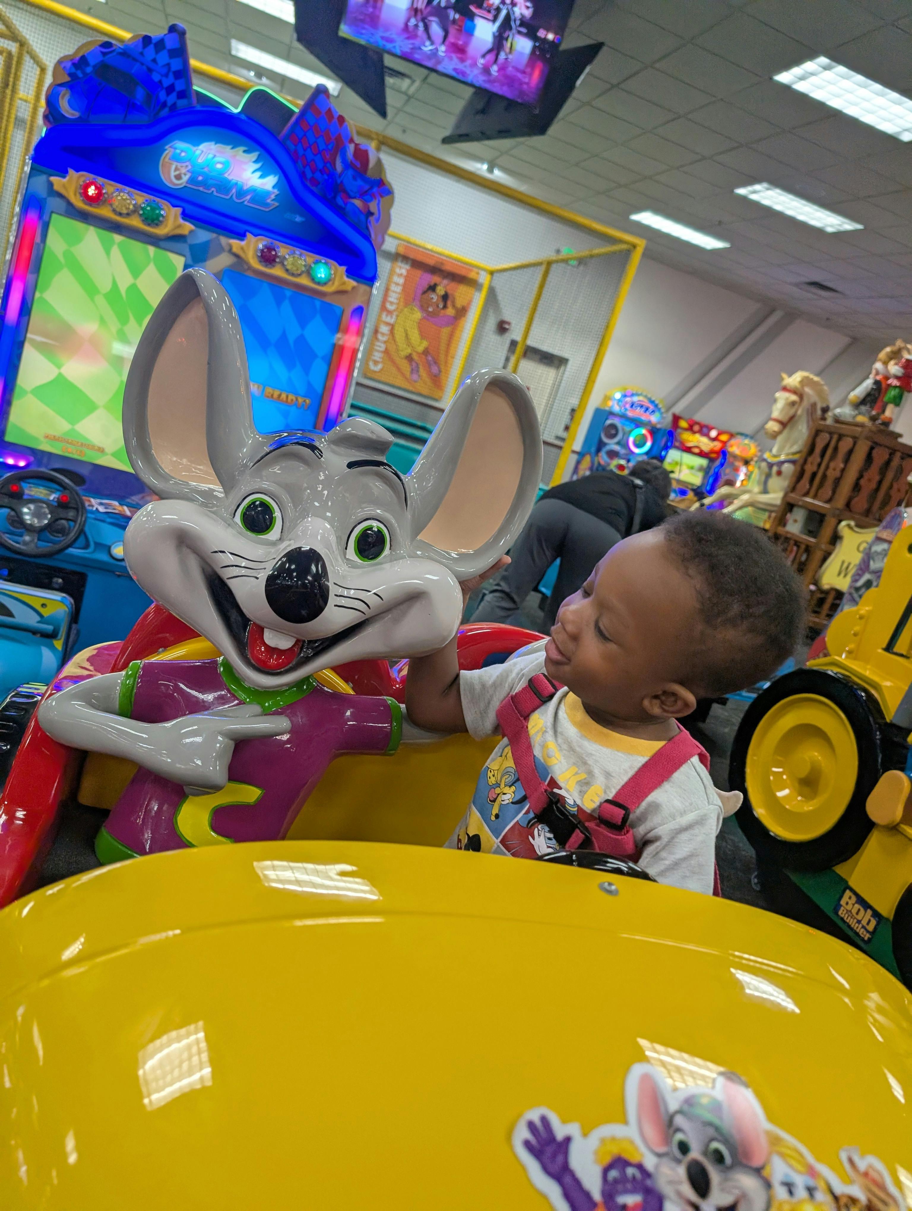 Child in a yellow ride-on toy next to a large mouse character