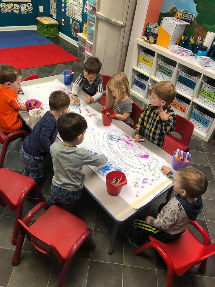 Children drawing on a large sheet of paper at a table in a classroom