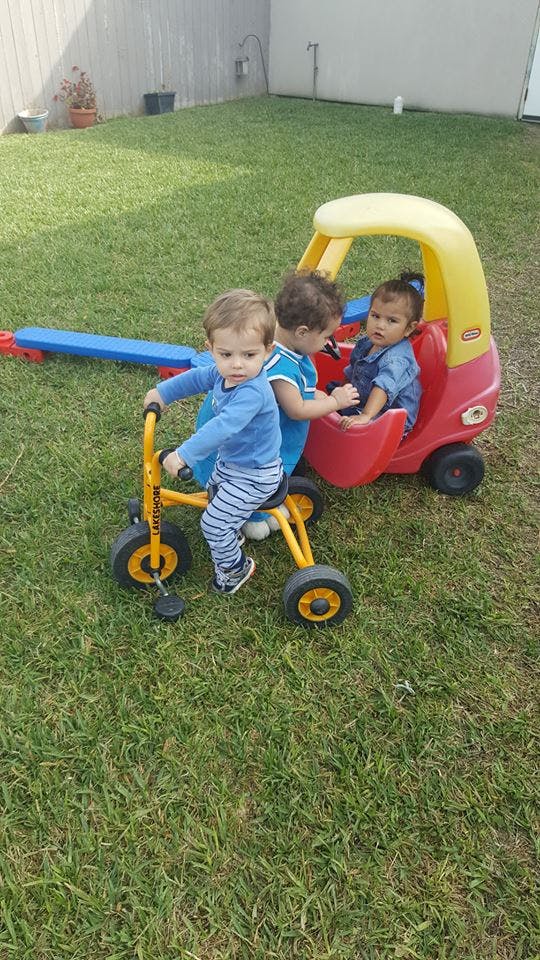Three children playing with a tricycle and a toy car on grass