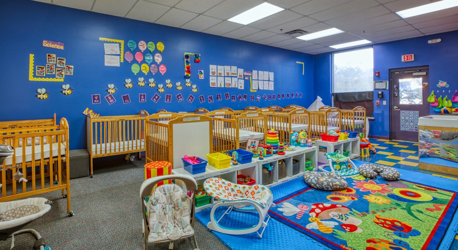 cribs in a childcare nursery classroom with colorful decorations and toys