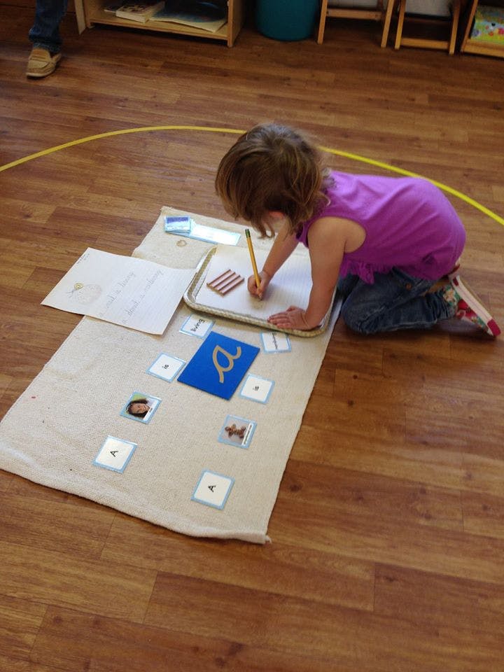 Child kneeling on floor, writing on paper with a pencil