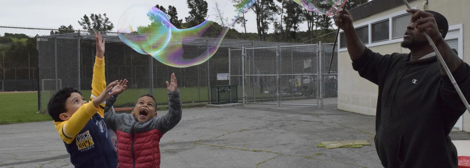 Person making large bubbles with two children reaching for them
