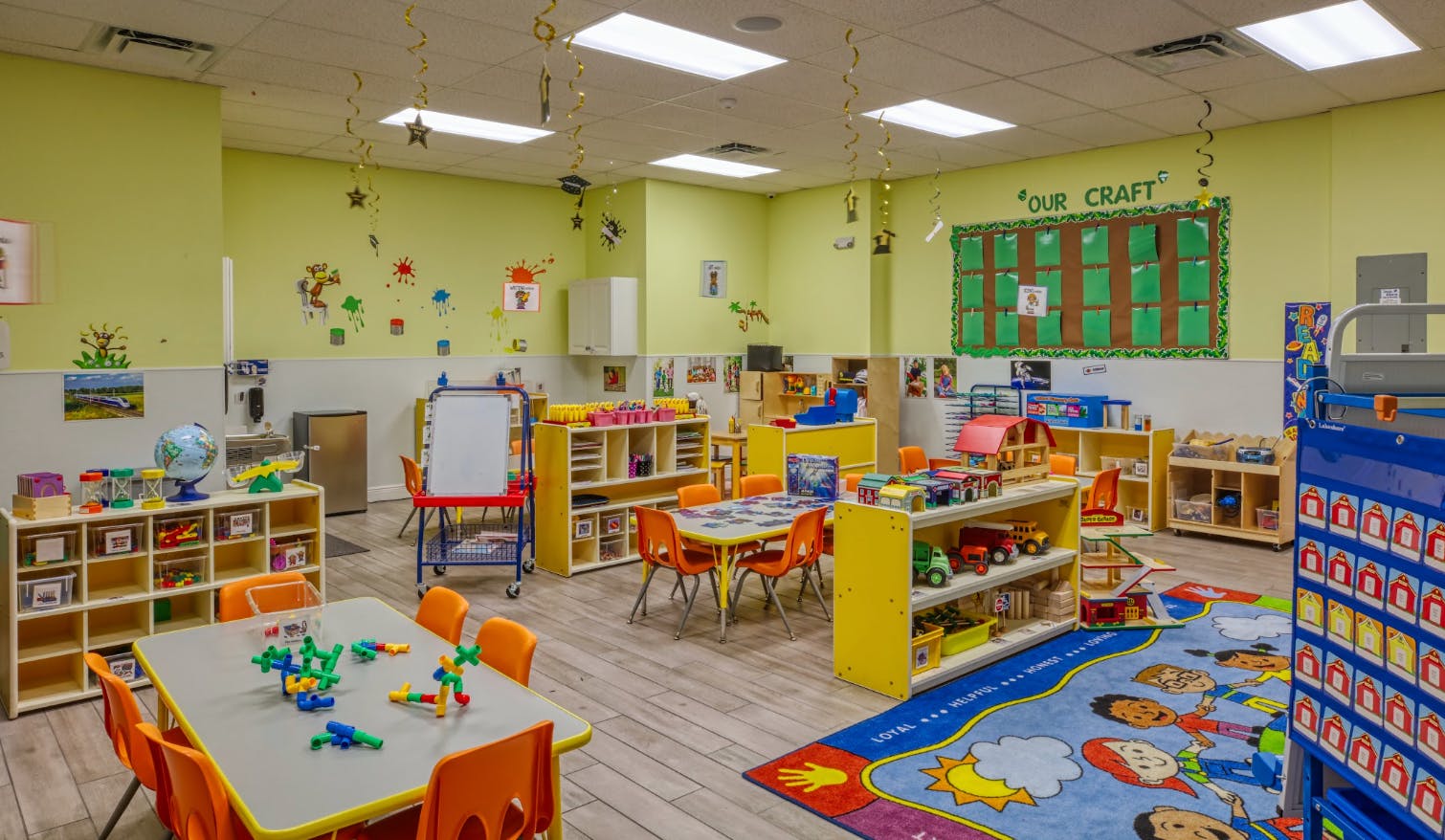A brightly lit classroom with small tables, chairs, and educational toys