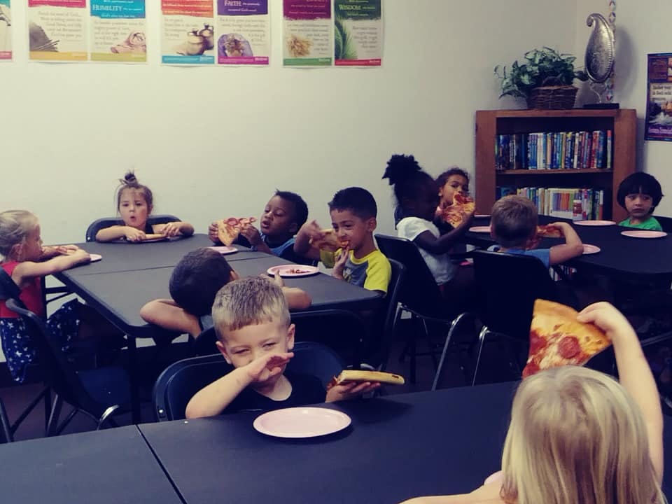 Children eating pizza at tables in a room