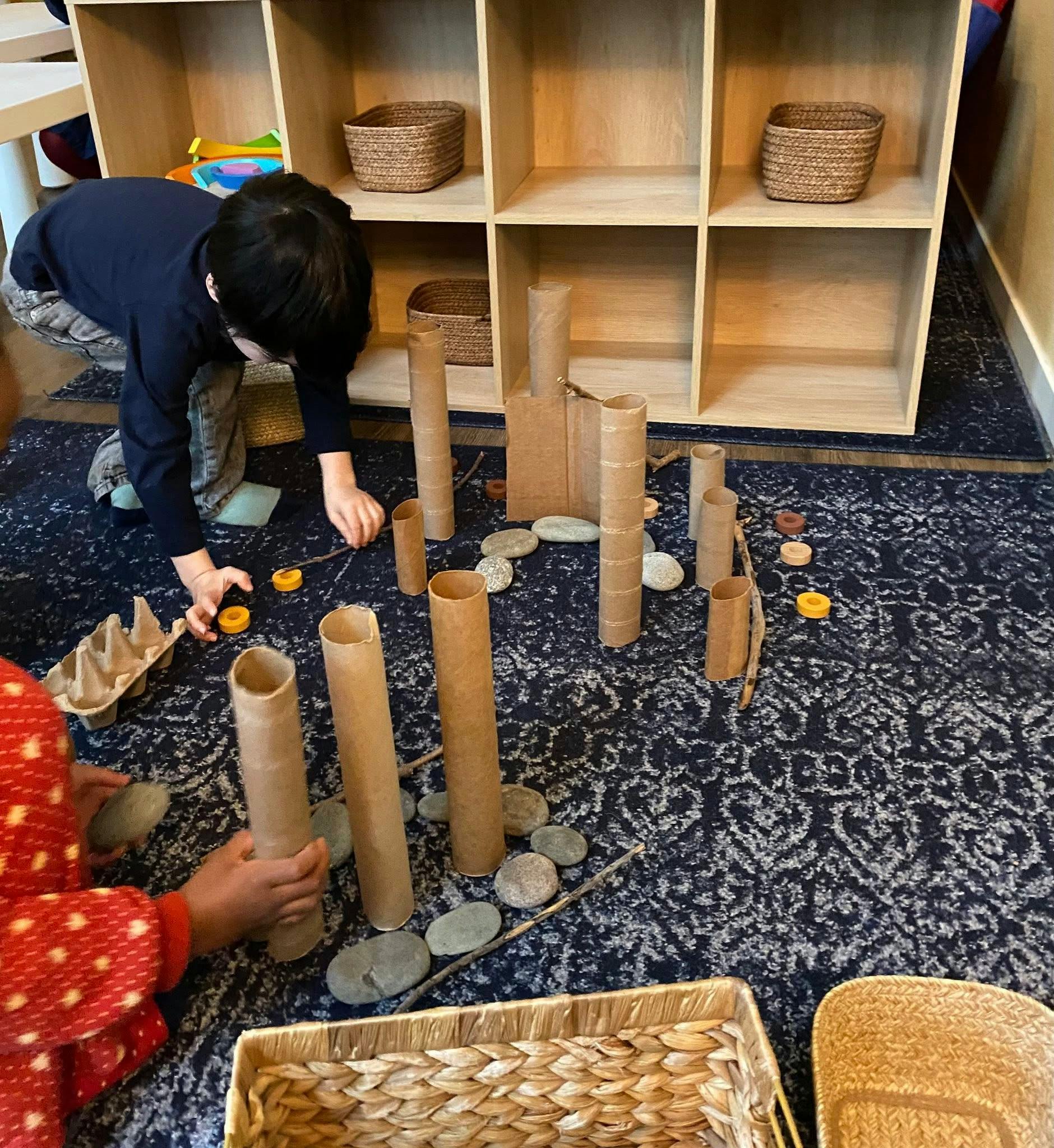 Two children playing with cardboard tubes and rocks on a rug