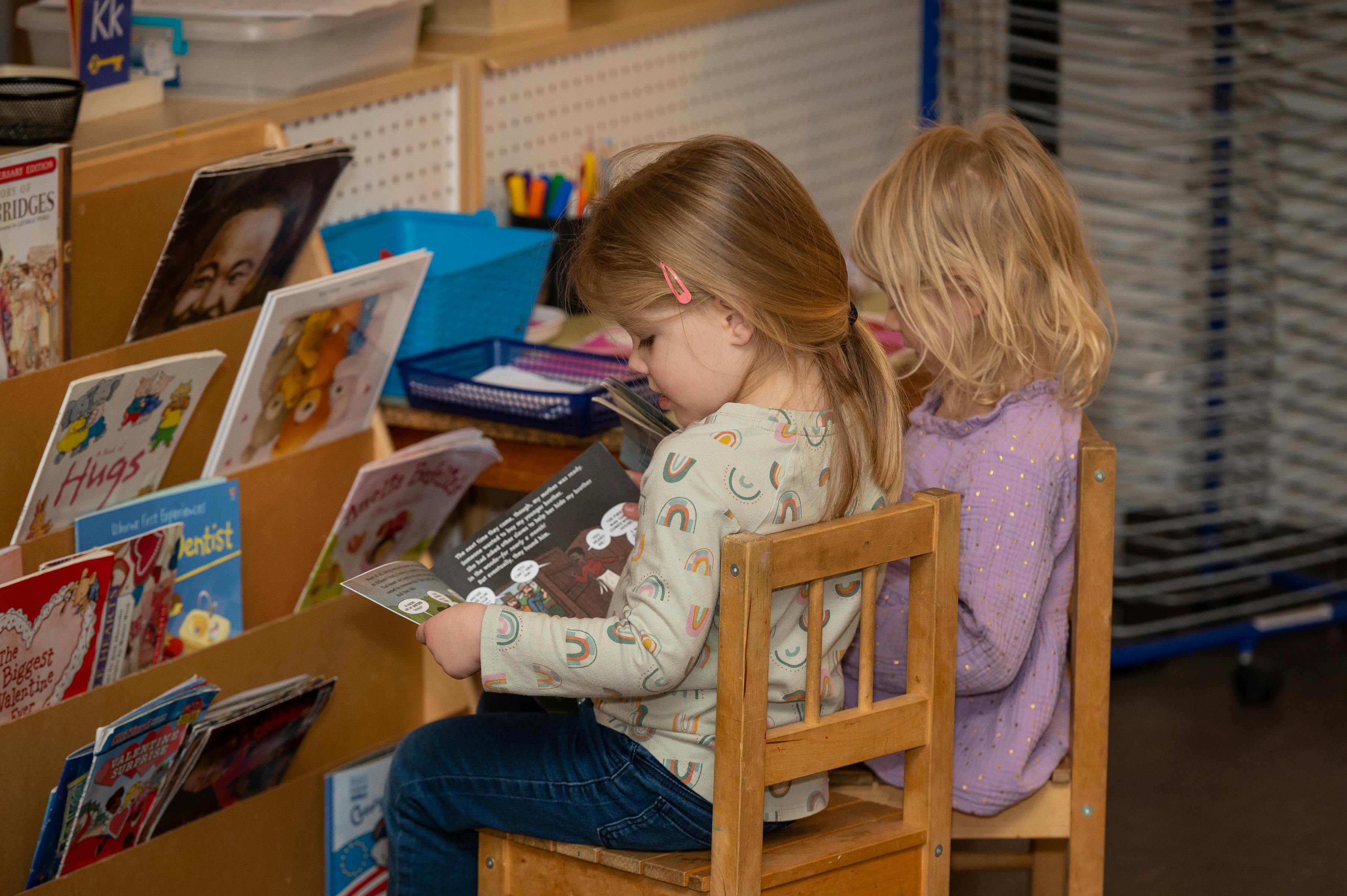Two children sitting in chairs, one reading a book
