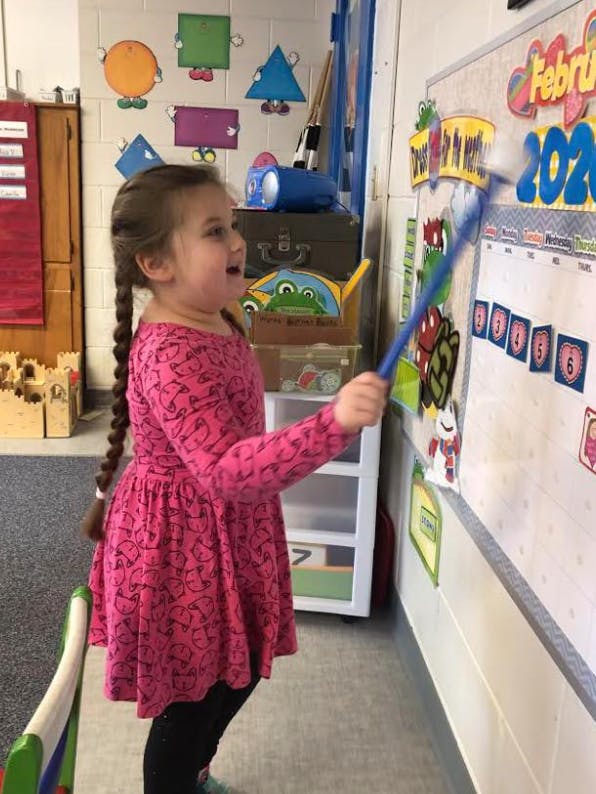 Child pointing at a calendar on a whiteboard with a stick