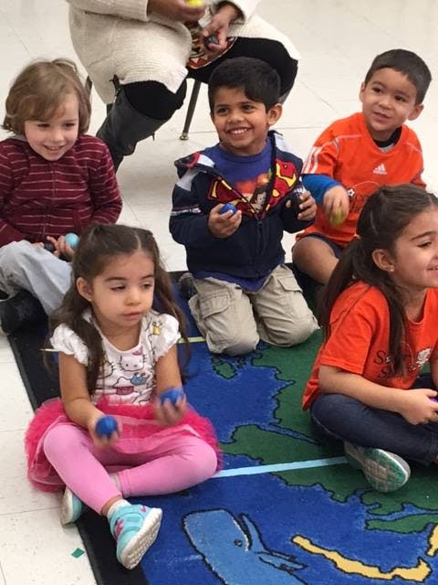 Five children sitting on a rug, some holding small balls