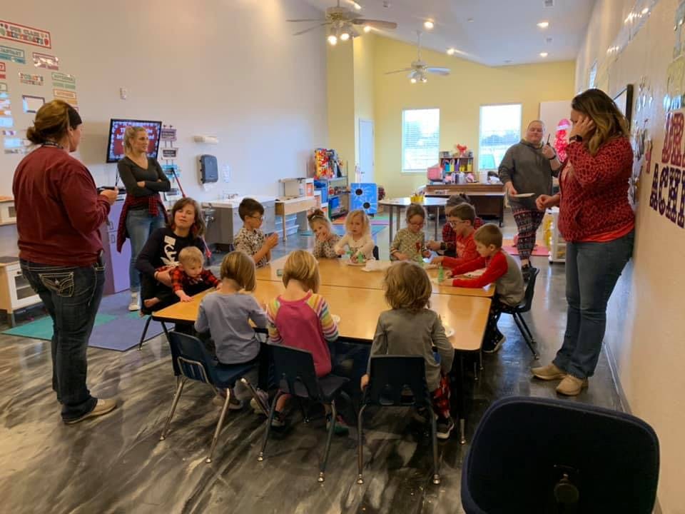 Adults and children gathered around tables in a classroom