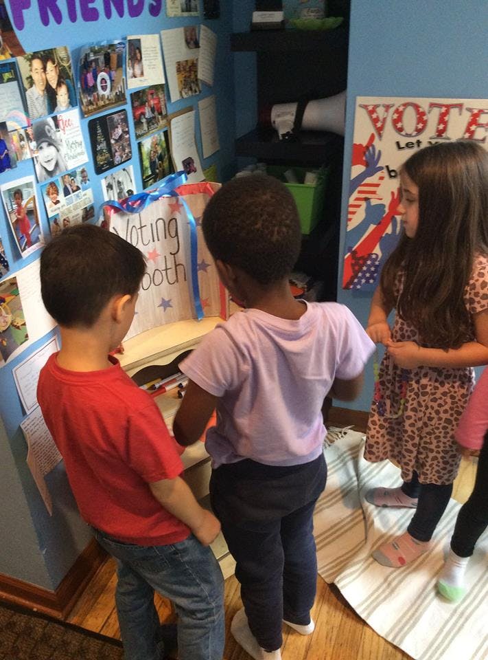 Three children looking at a "Voting booth" sign