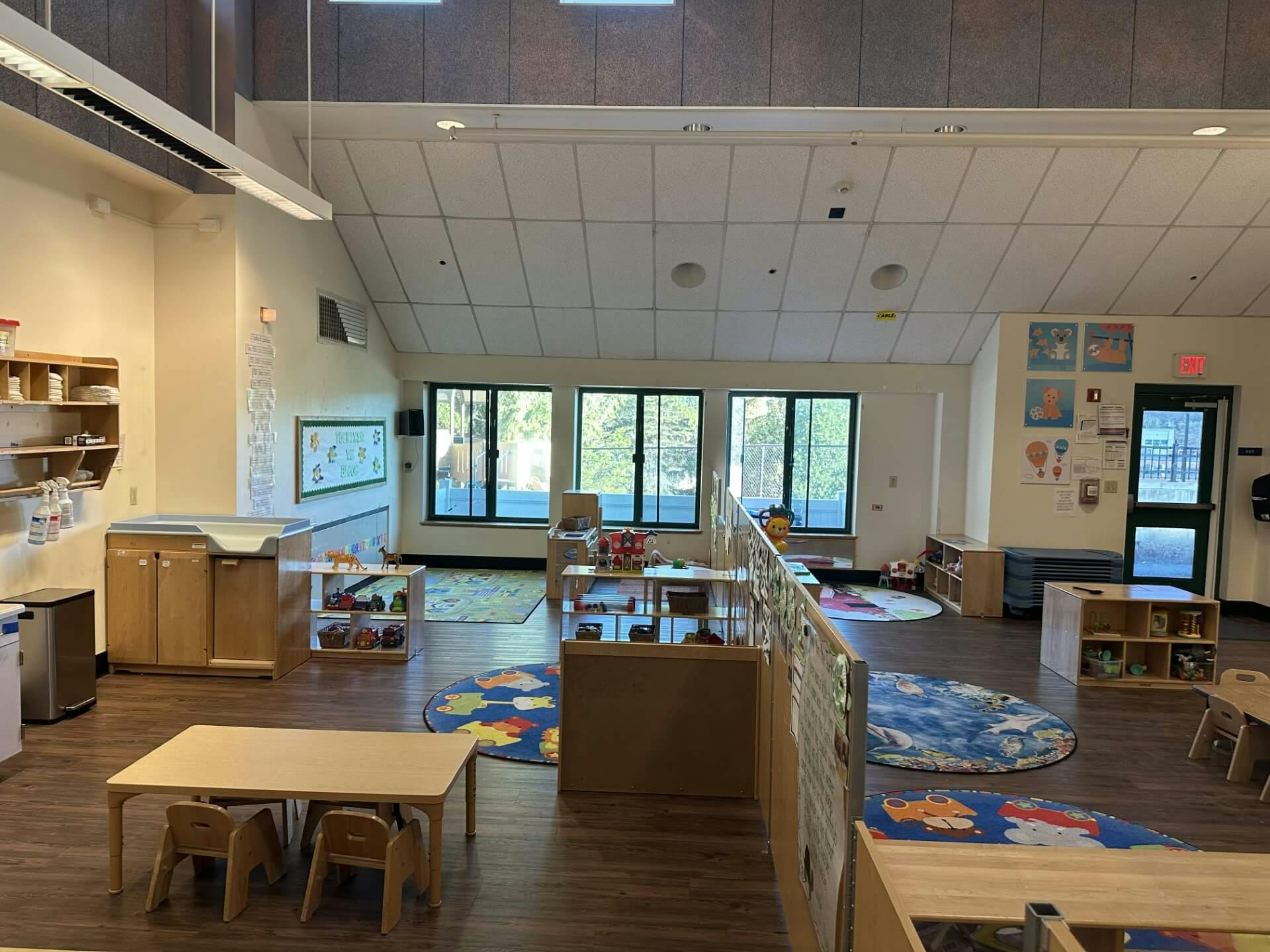 Empty classroom with small tables and chairs, play mats, and storage shelves