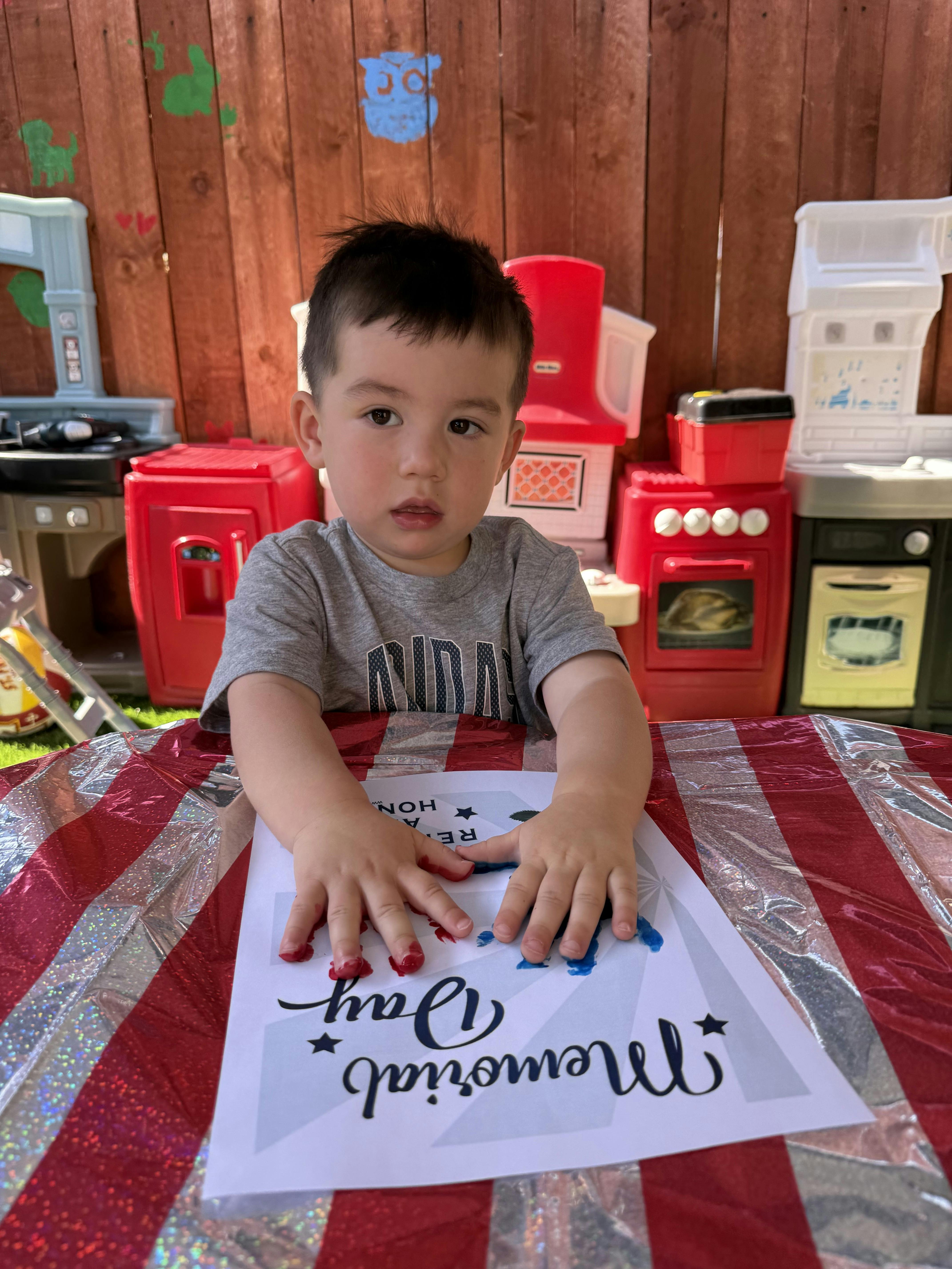 Child with red and blue paint on hands above "Memorial Day" craft