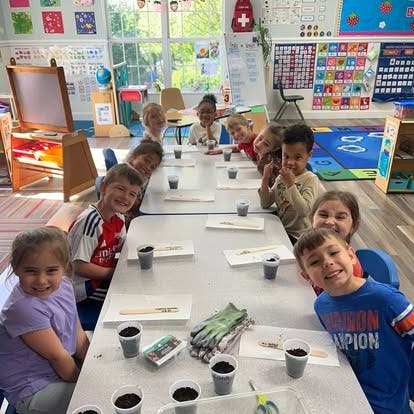 Group of children at tables in a classroom with planting supplies