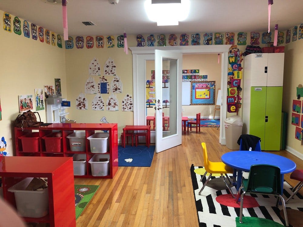 Empty classroom with small tables and chairs, storage units, and artwork on walls
