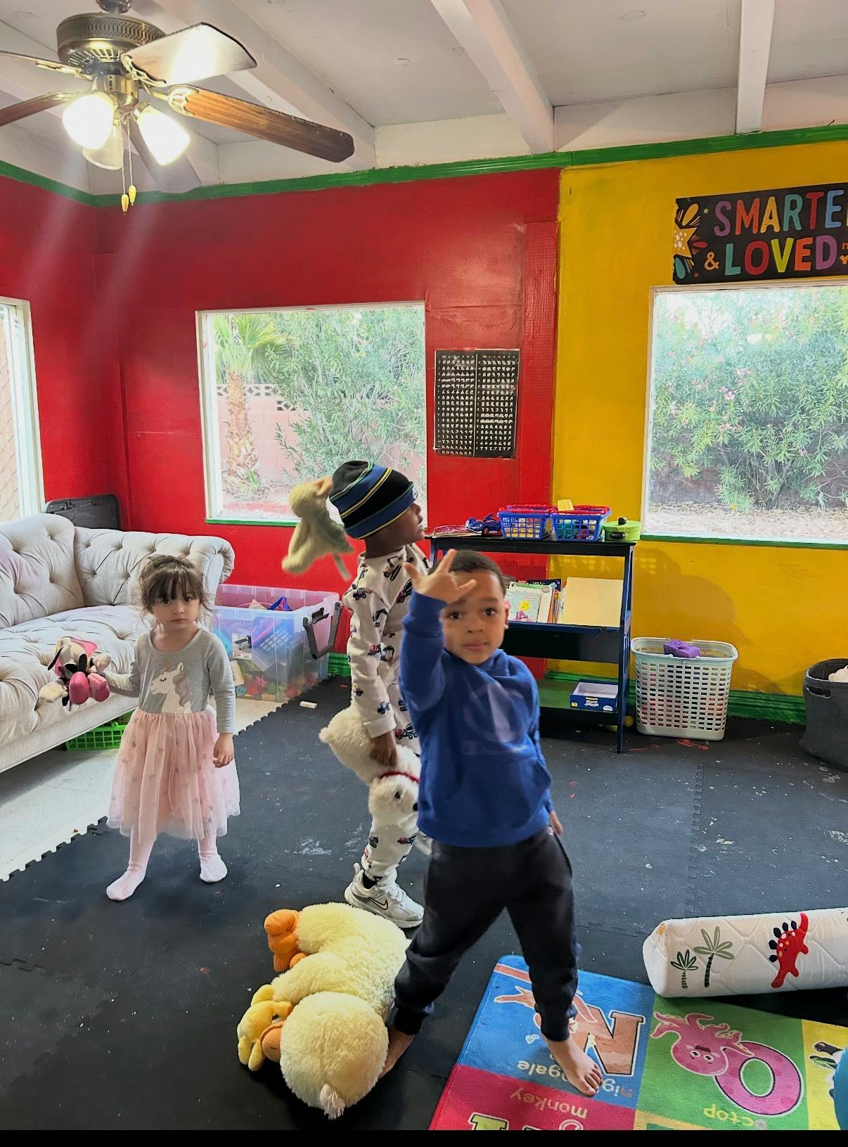 Three children in a colorful room, one holding up two fingers