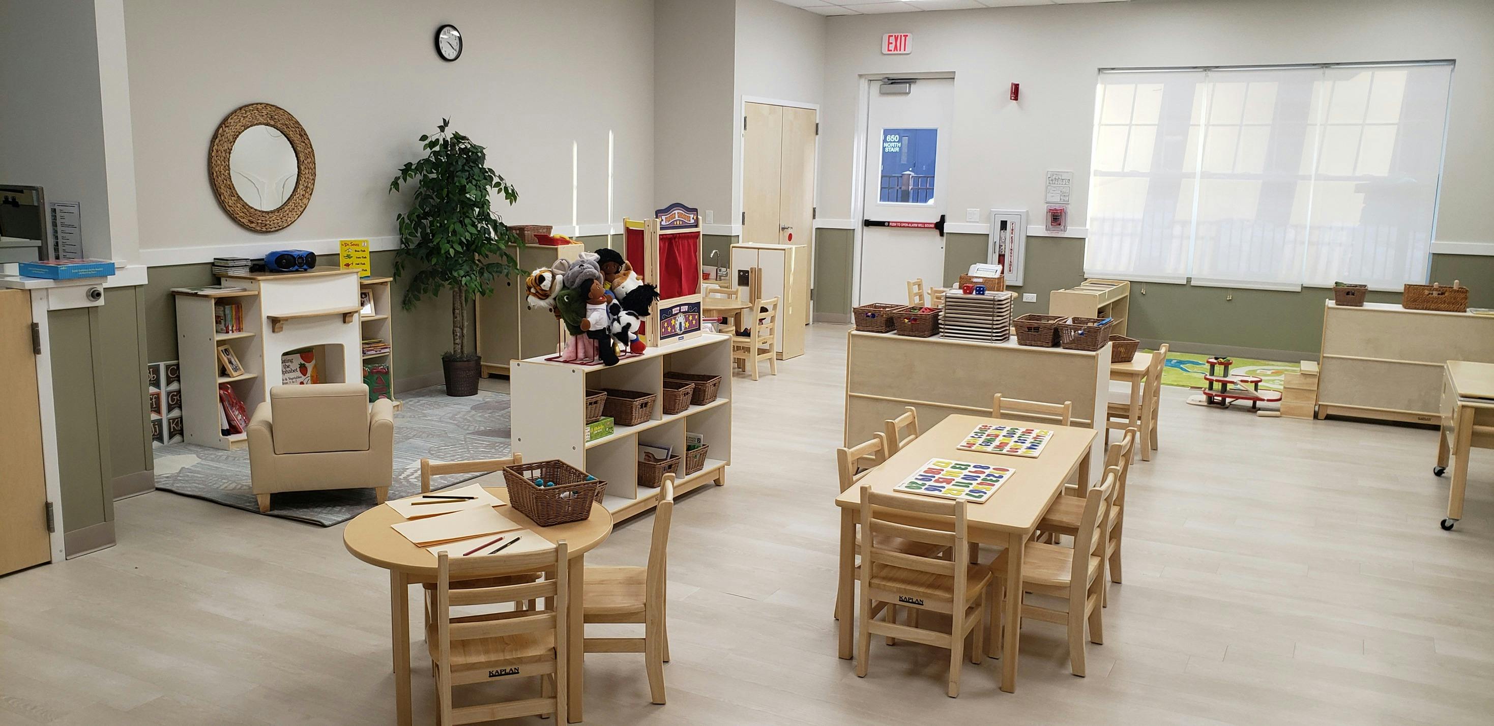 Classroom with small wooden tables and chairs, shelves, and a large window