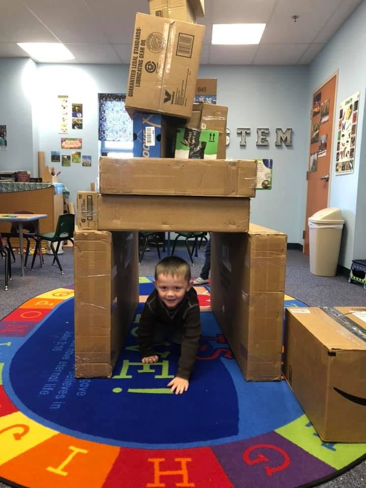 Child crawling through a fort made of cardboard boxes in a classroom
