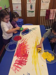 Children painting with rollers and brushes on a long sheet of paper