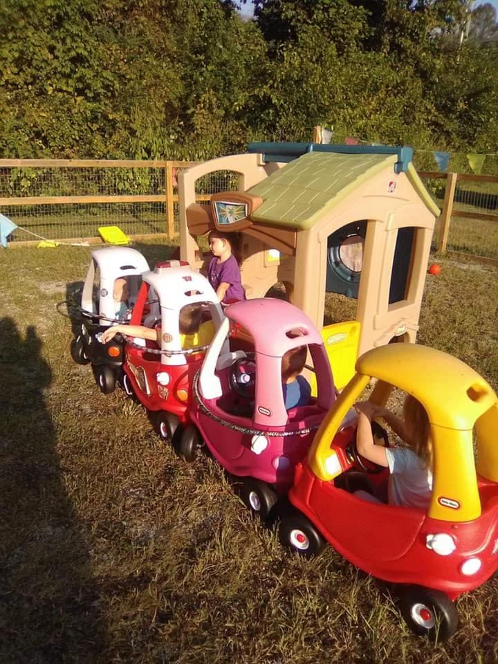 Children playing in toy cars and a playhouse outdoors