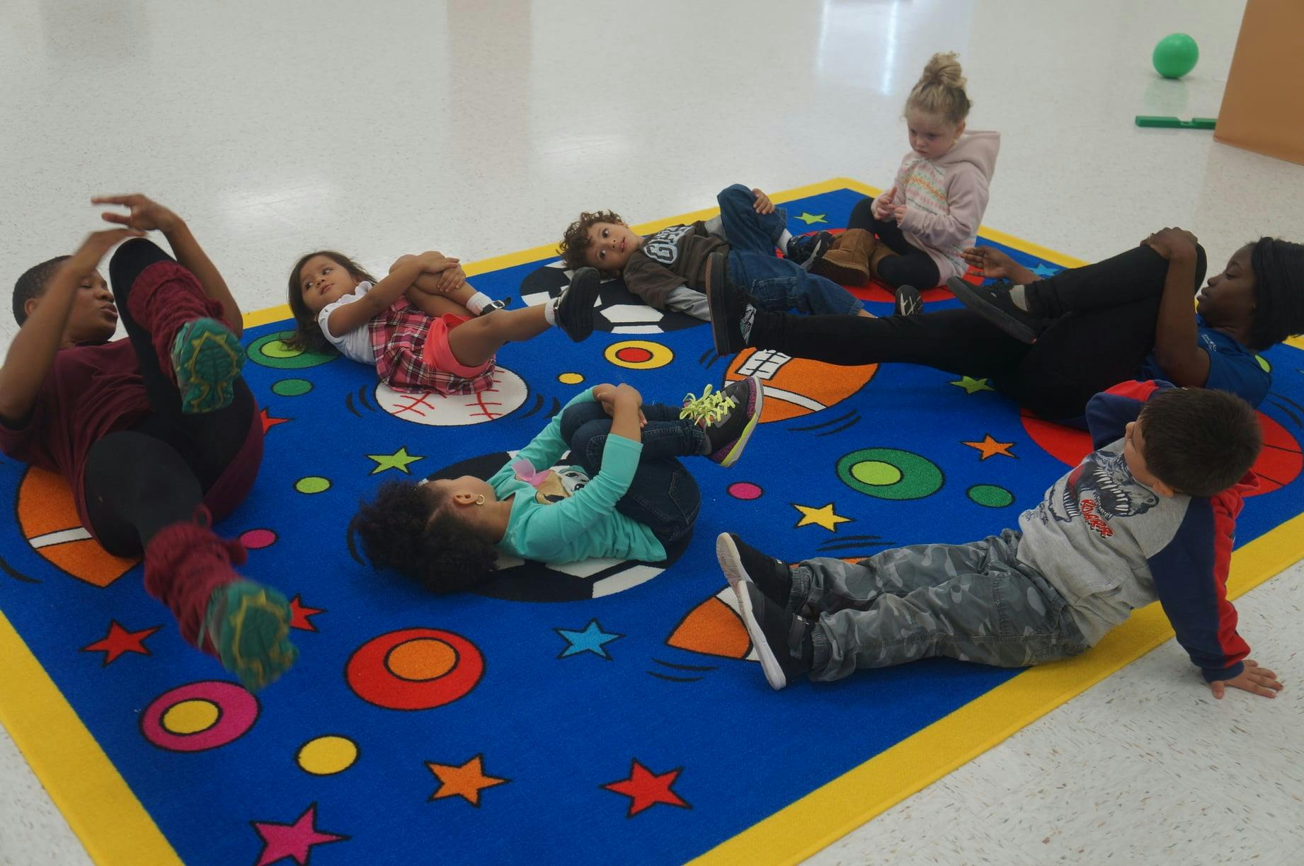 Children lying on a colorful rug, some with knees bent