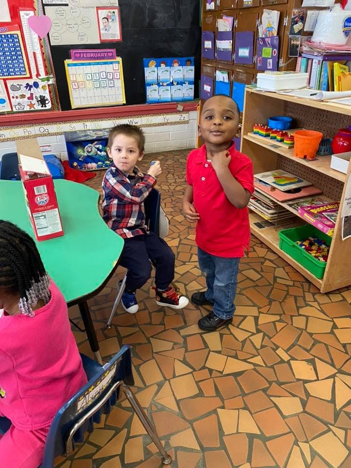 Two children in a classroom, one seated at a table and one standing