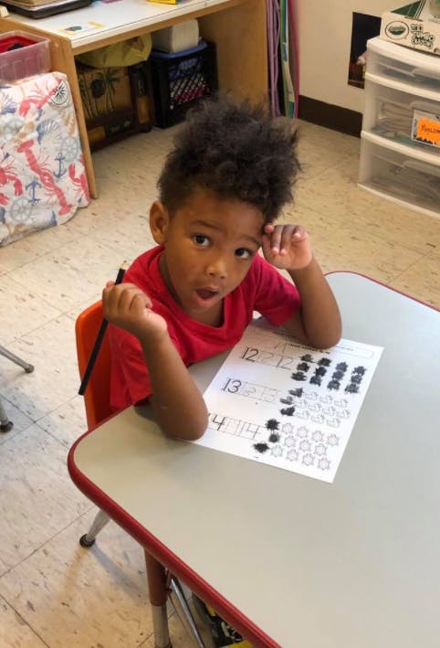 Child sitting at a desk with a pencil and a worksheet